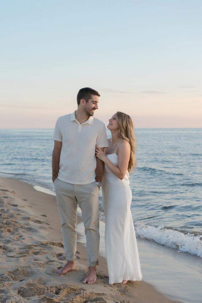Image of couple embracing and smiling at each other at golden hour on the shore at Oval Beach in Michigan.
